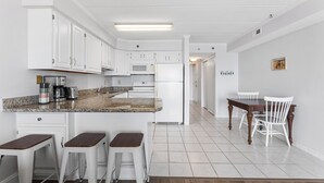 Une cuisine moderne avec des meubles blancs, un plan de travail en granit et un coin repas comprenant une table en bois et des chaises blanches.