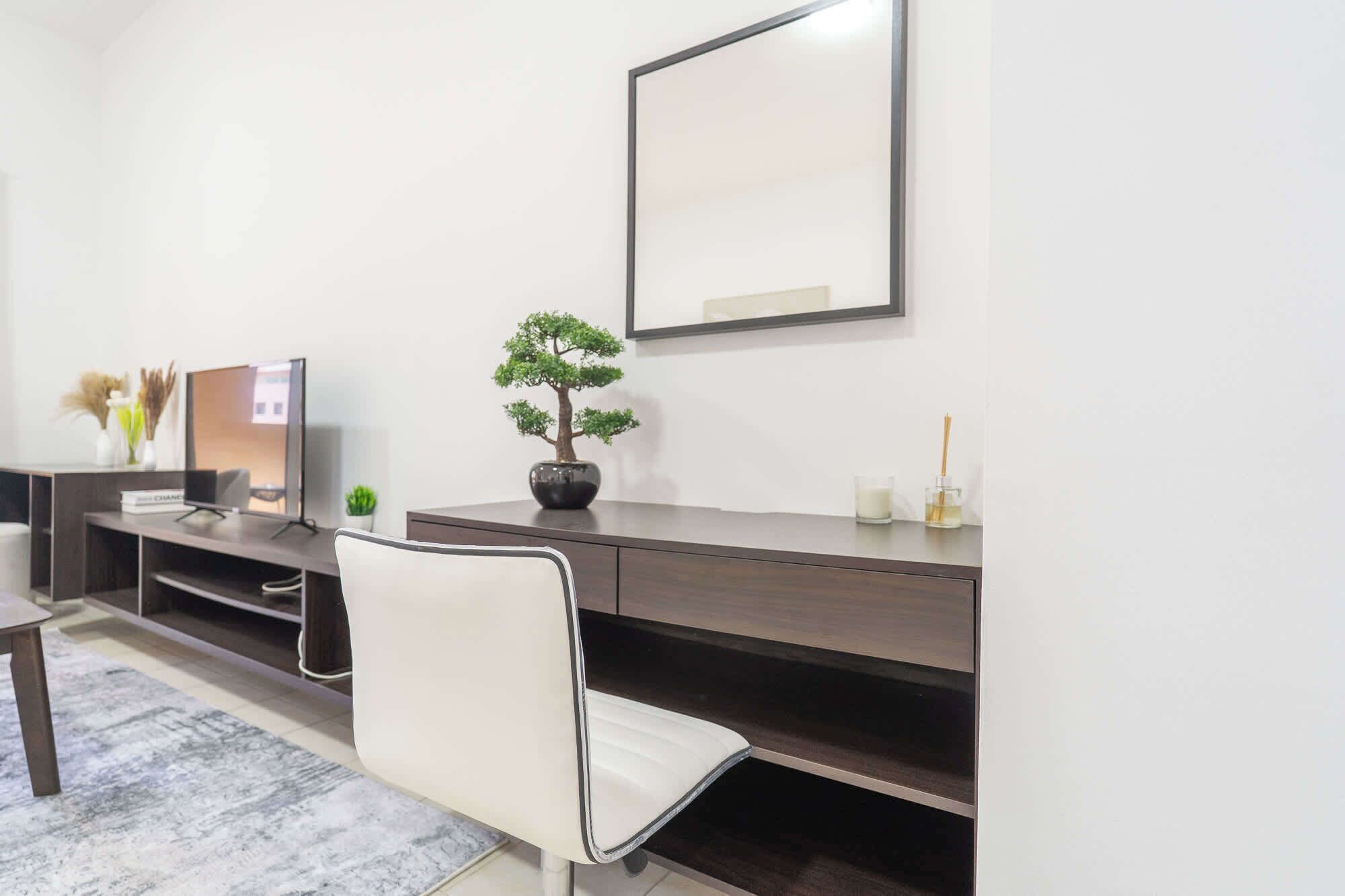 A modern living room with a dark wooden entertainment unit, a white sofa, a small potted plant, and a large mirror on the wall.
