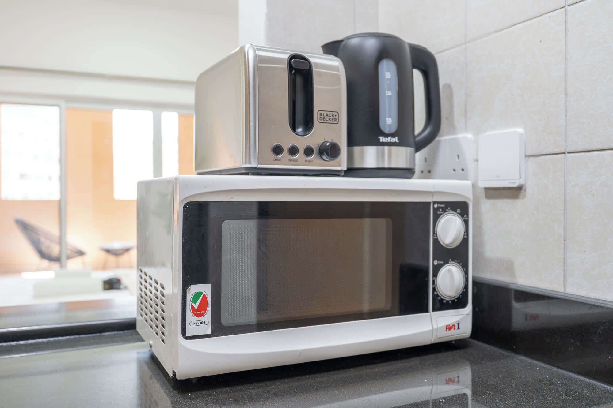 Un four à micro-ondes blanc doté d’un écran numérique et d’un panneau de commande, une machine à café noire et un petit logo sur le côté.