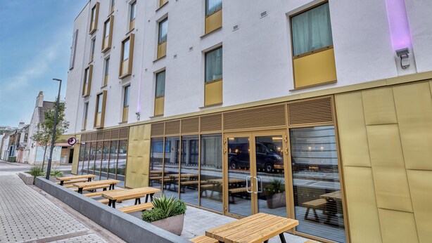A modern building with multiple windows, outdoor seating, and a reflective glass facade. - Premier Inn Jersey St Helier - Bath Street (St. Helier)