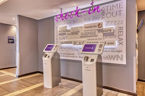 A hotel reception area with a check-in counter, a digital display, and a wall with motivational phrases. - Premier Inn Jersey St Helier - Bath Street (St. Helier)