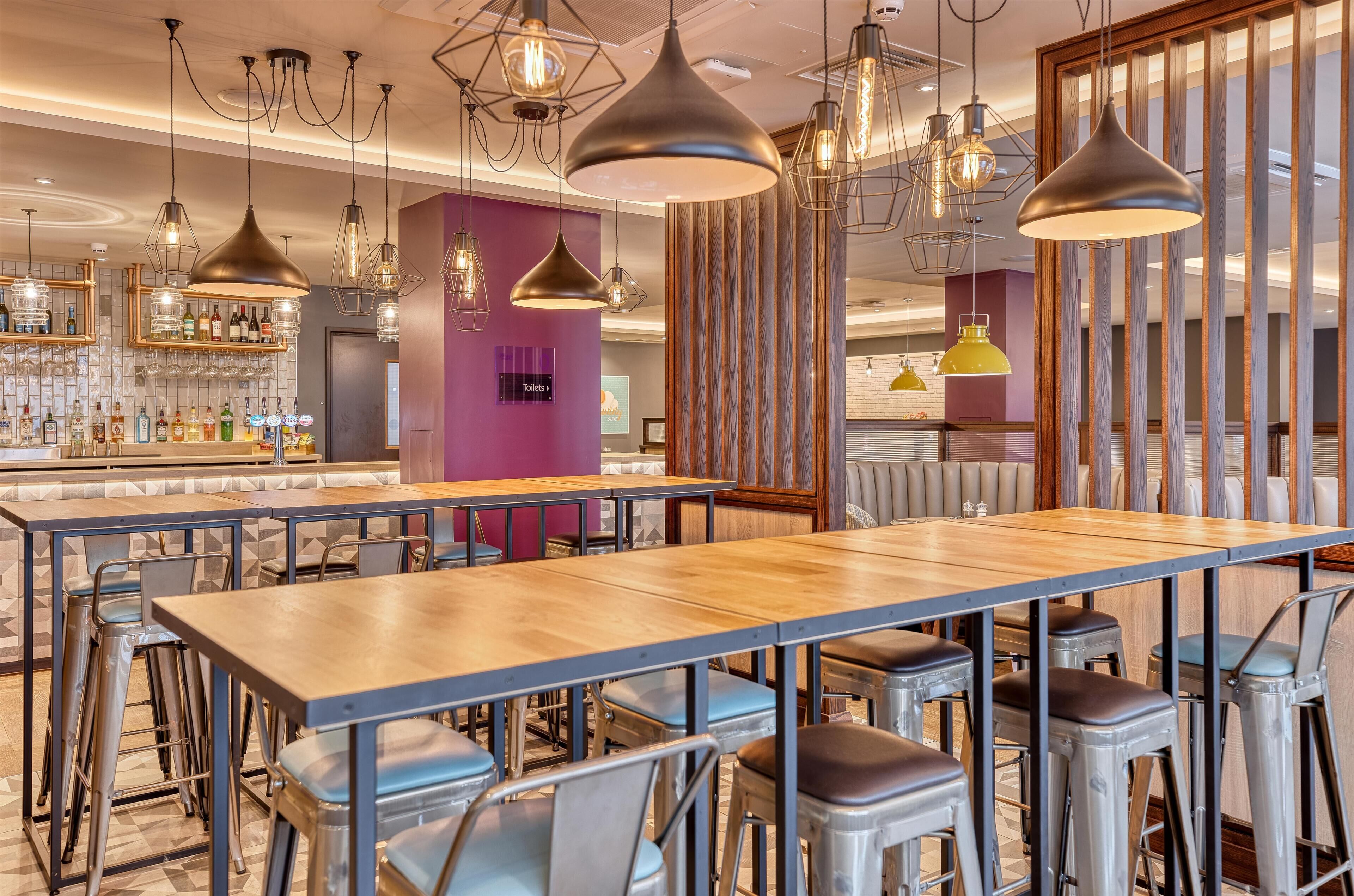 A modern bar area with multiple seating options, including bar stools and tables, and a variety of hanging pendant lights.