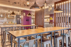 A modern bar area with multiple seating options, including bar stools and tables, and a variety of hanging pendant lights. - Premier Inn Jersey St Helier - Bath Street (St. Helier)
