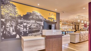 A reception area with a large wall mural, a counter with a digital screen, and a bar area with shelves of bottles. - Premier Inn Jersey St Helier - Bath Street (St. Helier)