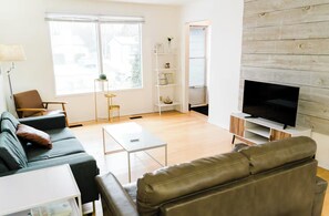 A modern living room with a sofa, coffee table, TV, and a bookshelf.