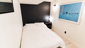 A bedroom with a white bed, a black brick accent wall, a nightstand with a lamp, and a painting on the wall.