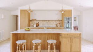 A modern kitchen with a central island, three wicker stools, wooden cabinets, and pendant lighting.