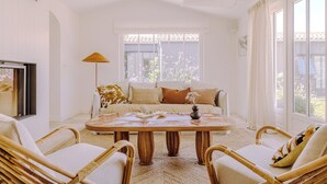 A bright living room with a sofa, two wicker chairs, a round wooden table, and a floor lamp.