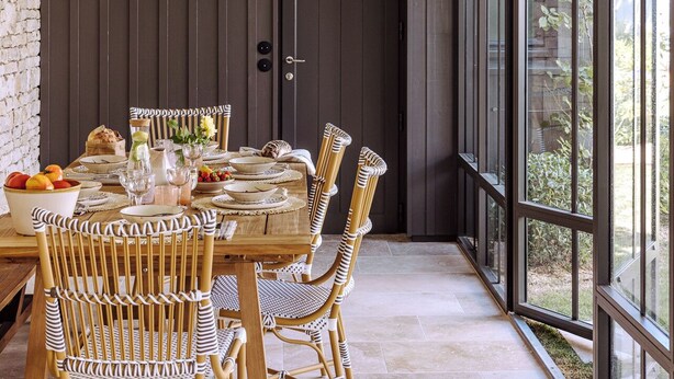 A dining area with a long table, wicker chairs, and hanging light fixtures.
