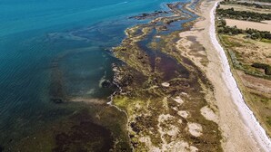 An aerial view of a coastal area with a sandy beach, clear blue waters, and a distant shoreline.