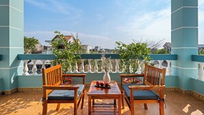 Une terrasse avec des meubles en bois, un vase rempli de fleurs et une vue sur des bâtiments en arrière-plan.