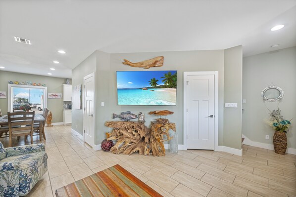A spacious living room with a large flat-screen TV, wooden decor, and a dining area with a view of the beach.