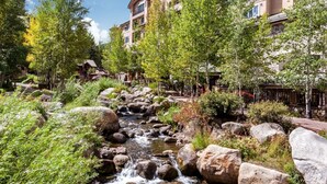 A hotel with a natural stream running through a landscaped garden, surrounded by trees and large rocks. - Contemporary 3 Bedroom Ski In, Ski Out Condo in the Heart of Beaver Creek Village (Avon)