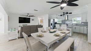 Een moderne keuken met witte kastjes, een eettafel gedekt voor vier personen en plafondventilatoren.