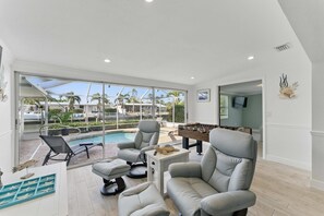 A spacious living area with a pool view, comfortable seating, and a foosball table.