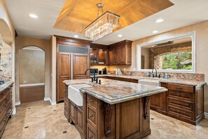 A spacious kitchen with a large island, wooden cabinetry, and a modern chandelier.