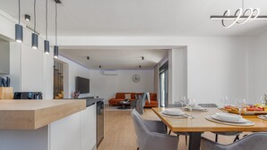 A modern kitchen with a wooden countertop and built-in appliances, a dining area with a wooden table and grey chairs, and a living area with a sofa and TV. - Villa Roma Murvica Zadarvillas (Policnik)
