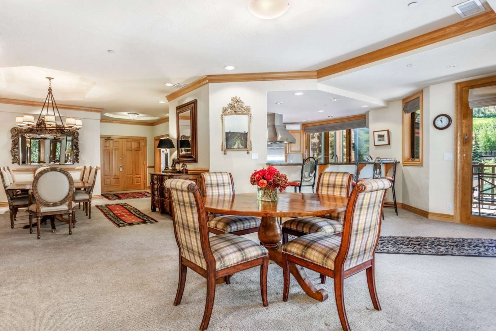 A dining area with a wooden table and plaid chairs, a chandelier, and a large mirror on the wall.