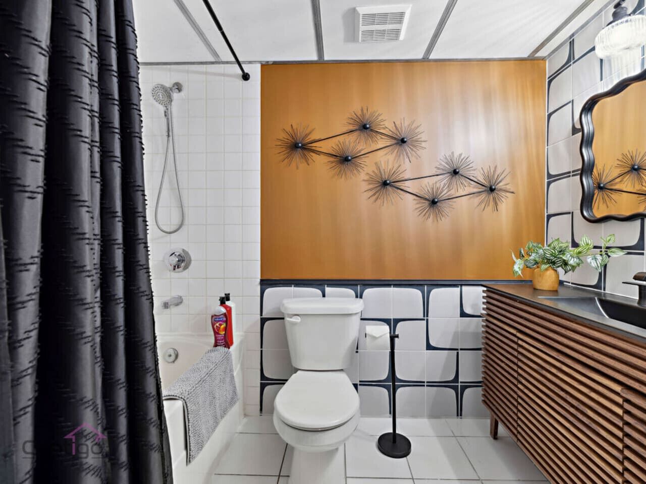 A modern bathroom with a white toilet, black and white tiled walls, a wooden vanity, and a shower with black curtains.