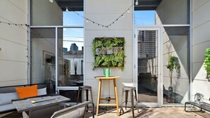 An outdoor patio with a sofa, table, and chairs, a green plant wall, and a city view.