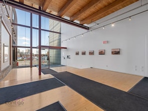 An art gallery with wooden floors, large windows, and paintings on the walls.