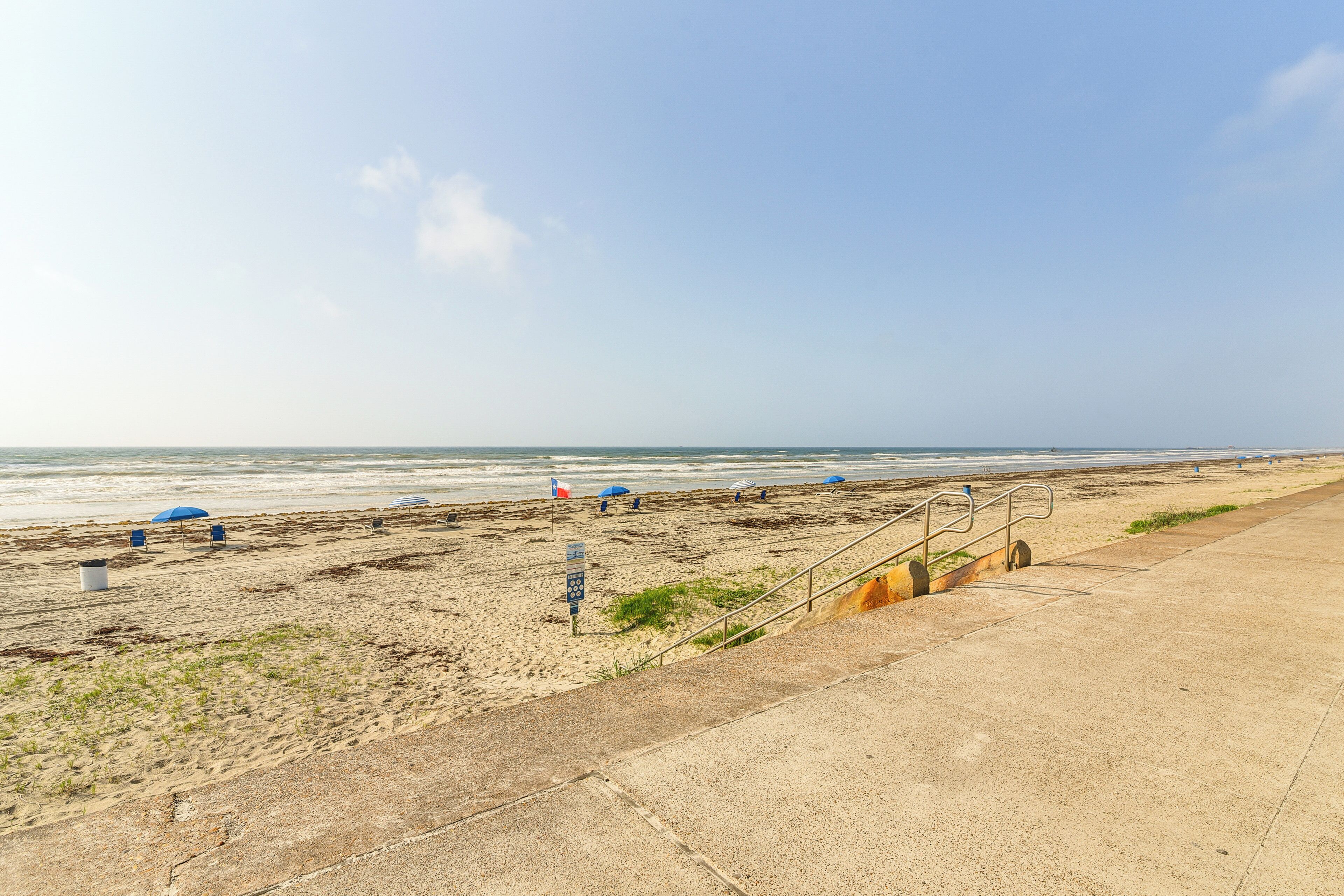 Ein Strand mit einer Betonpromenade, Sonnenschirmen und einer Flagge.