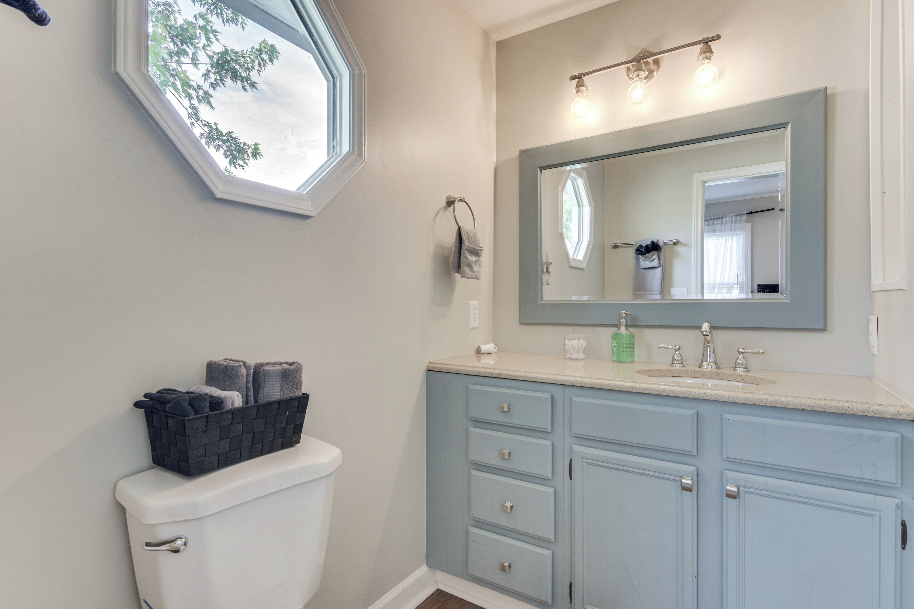A bathroom with a toilet, a sink with a mirror above it, and a window.