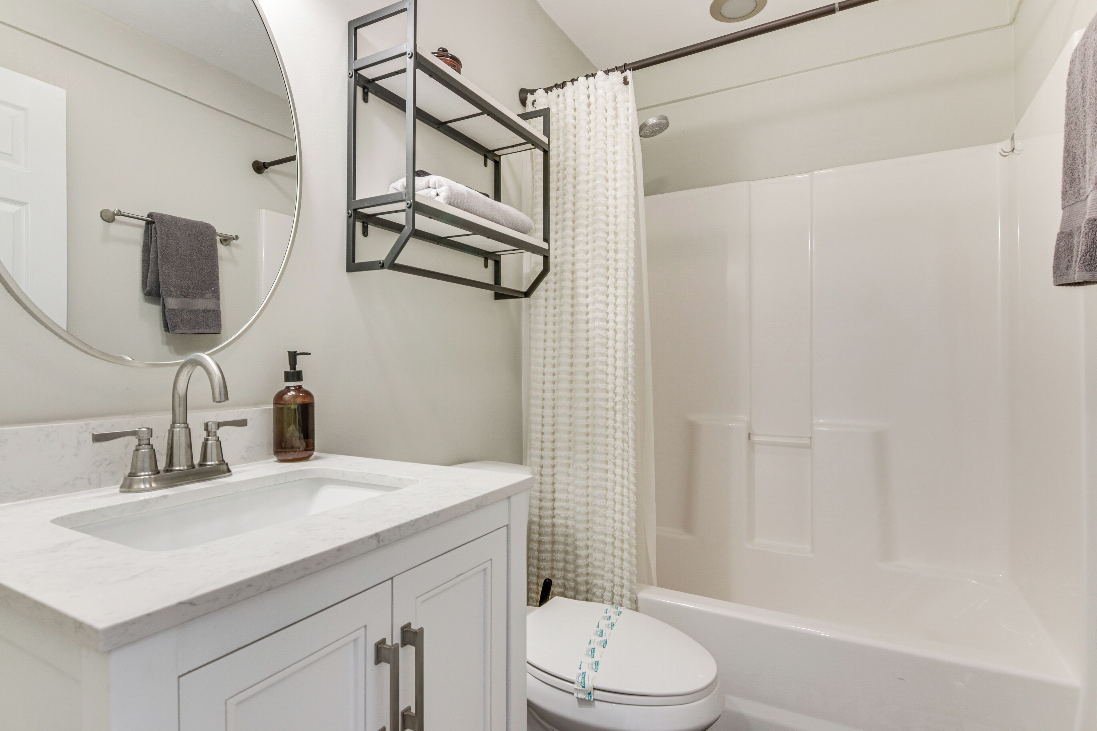 A bathroom with a white sink, a toilet, a shower with a white curtain, and a mirror with a towel hanging on the wall.