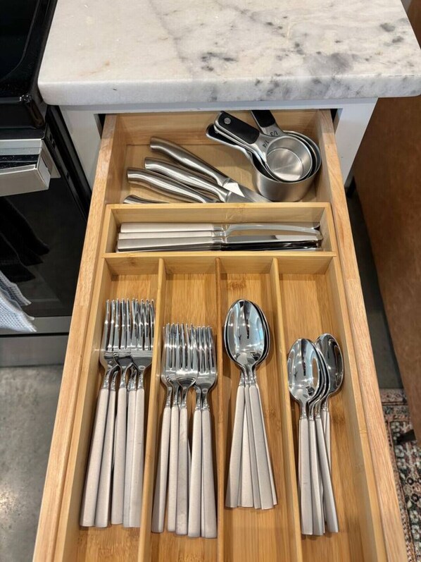 Un cajón de cocina con utensilios de cocina ordenados, incluyendo tenedores, cucharas y una espumadera.
