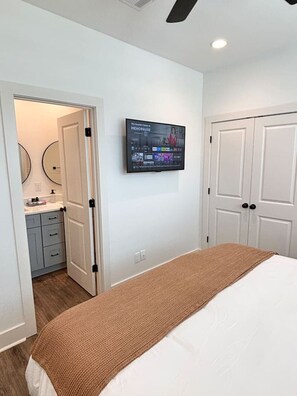 Un dormitorio con cama, televisor montado en la pared, armario y baño visible a través de una puerta abierta.