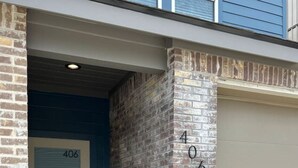 Entrada de un edificio con una puerta azul marcada con el número 406, un muro de ladrillo y una puerta de garaje.