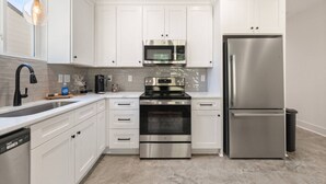 Una cocina moderna con armarios blancos, electrodomésticos de acero inoxidable, lavavajillas y cafetera.