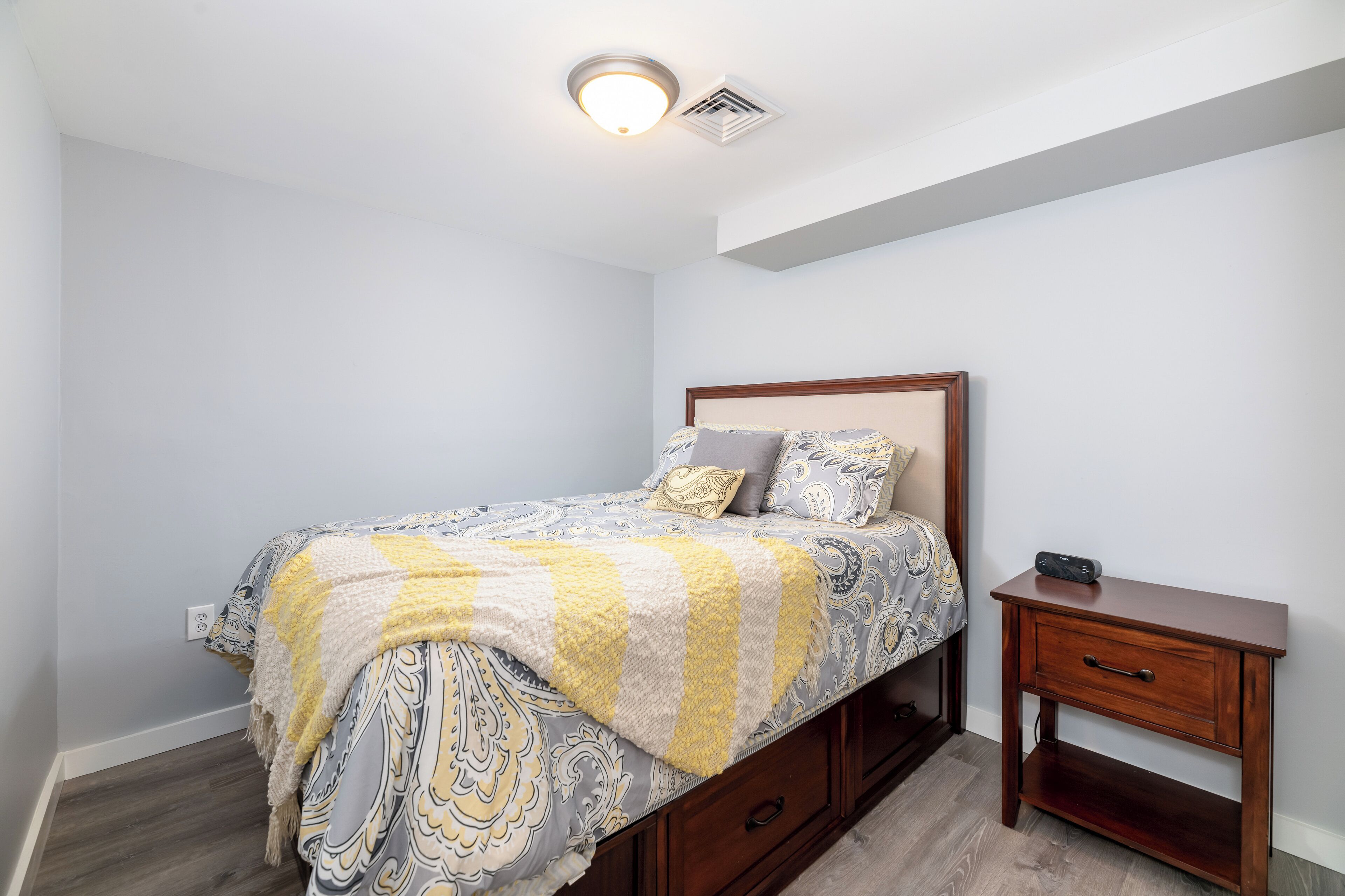 A bedroom with a bed, bedside table, and a ceiling light fixture.