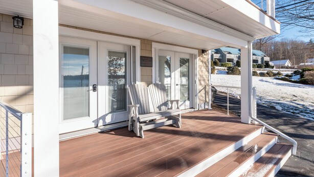 A covered porch with a white bench, a welcome sign, and a view of a snowy landscape.