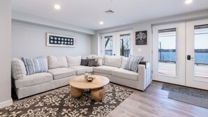 A modern living room with a light gray sectional sofa, a round wooden coffee table, and a patterned rug.
