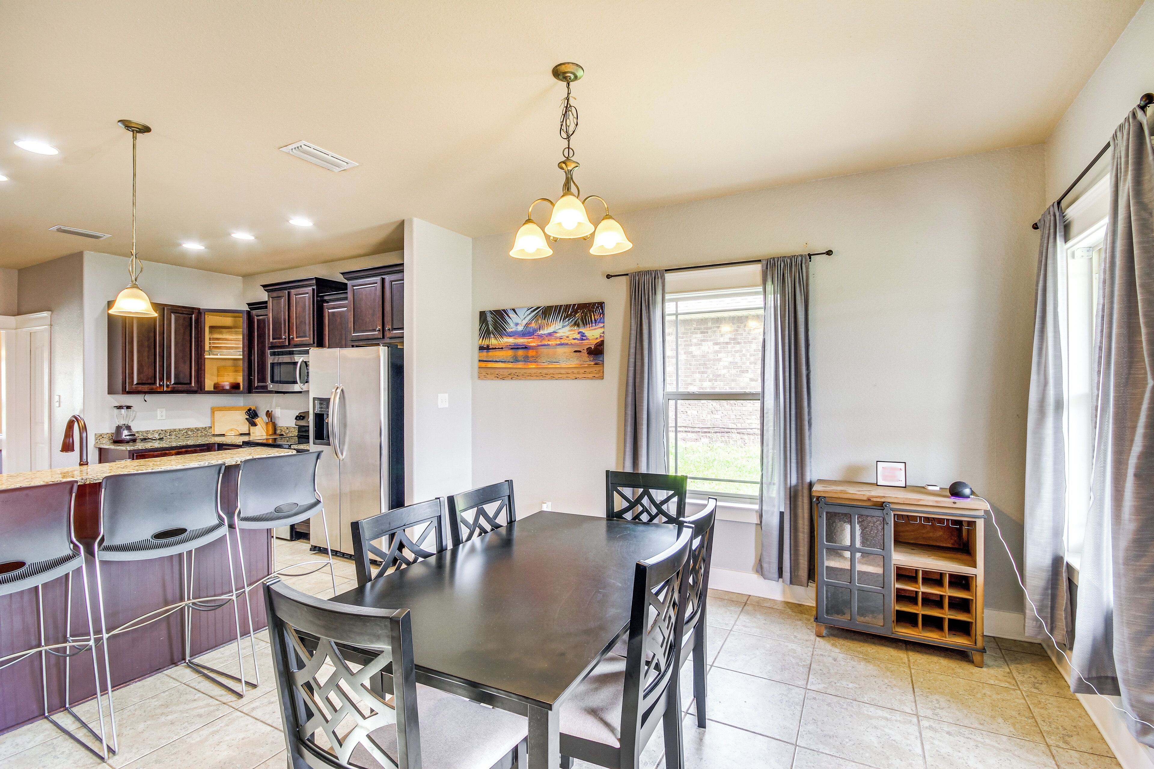 A modern kitchen with a dining area, featuring a central island, bar stools, and a pendant light.