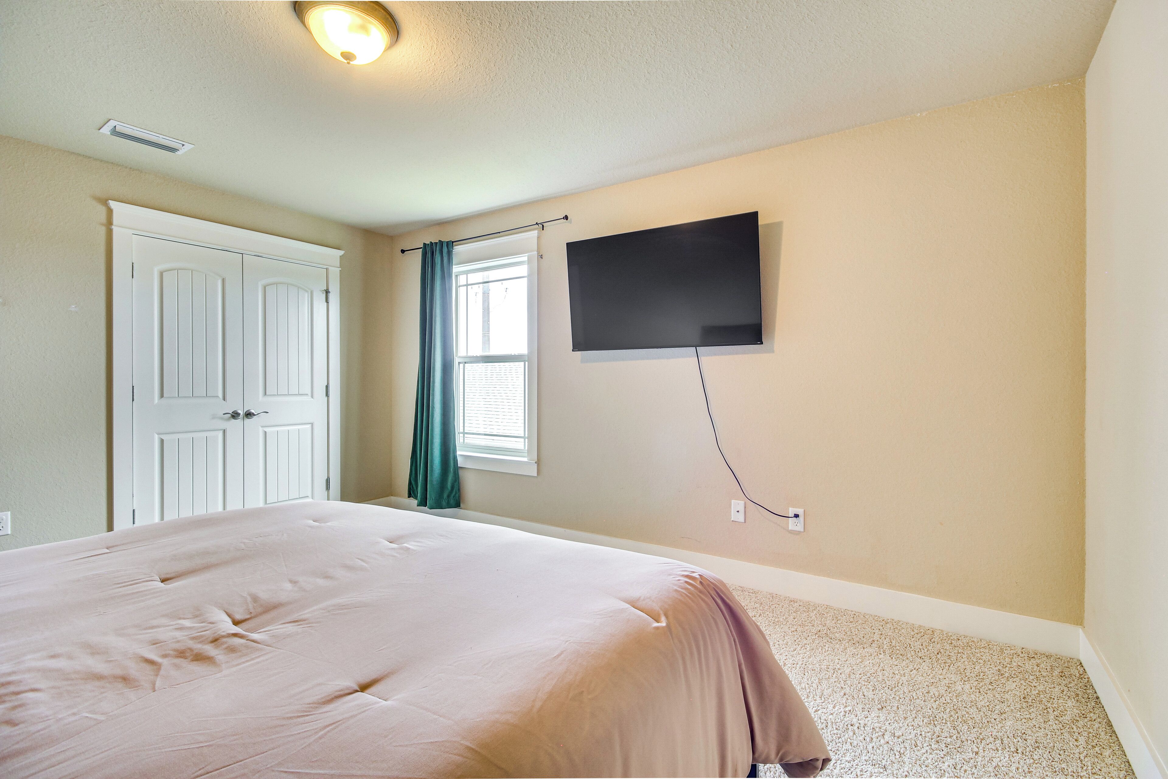 Una camera da letto con un letto, una televisione a parete, una finestra con tende e una porta.