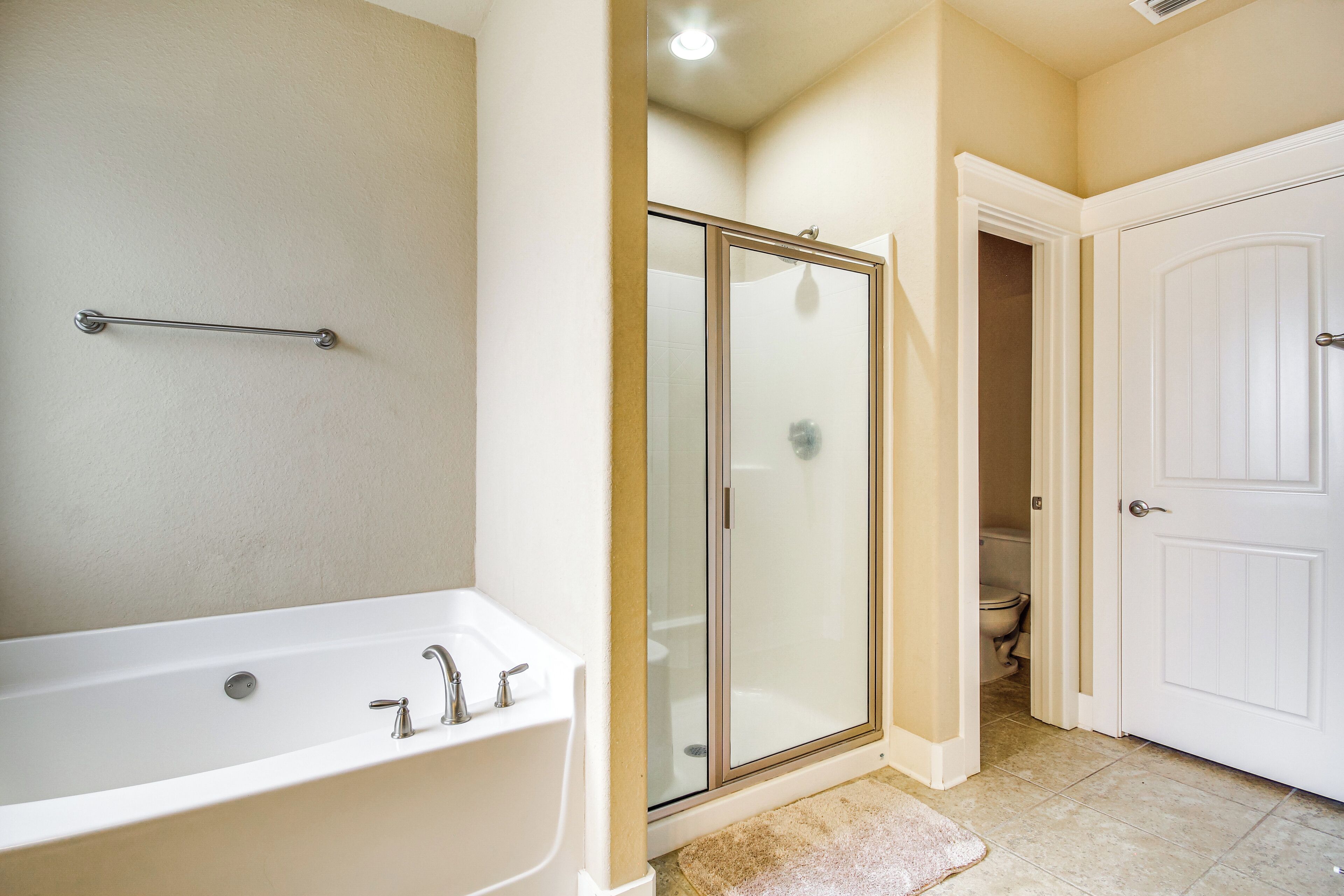 A bathroom with a bathtub, a glass-enclosed shower, and a toilet visible through an open door.
