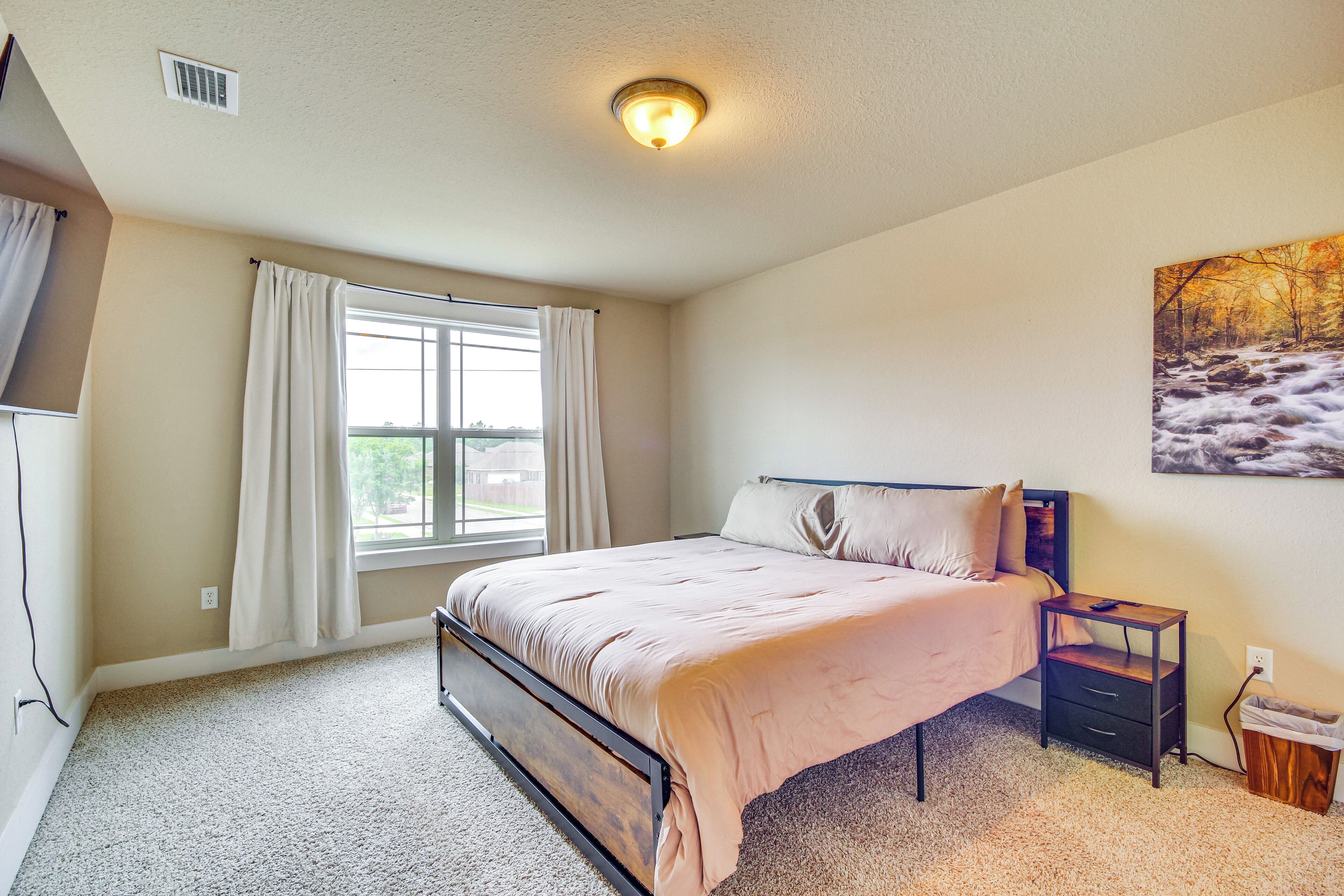 A bedroom with a bed, a nightstand, a window with curtains, and a painting on the wall.