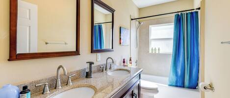 A bathroom with two sinks, a large mirror, a bathtub, and a shower curtain.