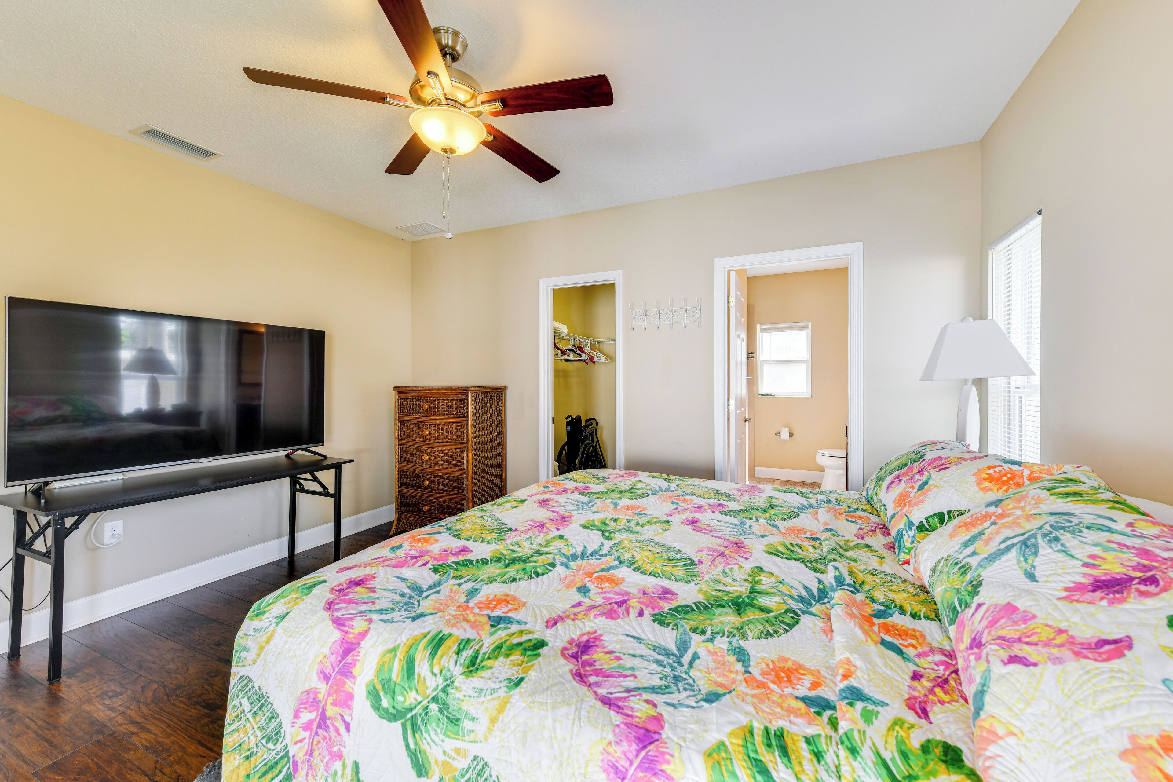 A bedroom with a large bed, a television, a ceiling fan, and a wardrobe.