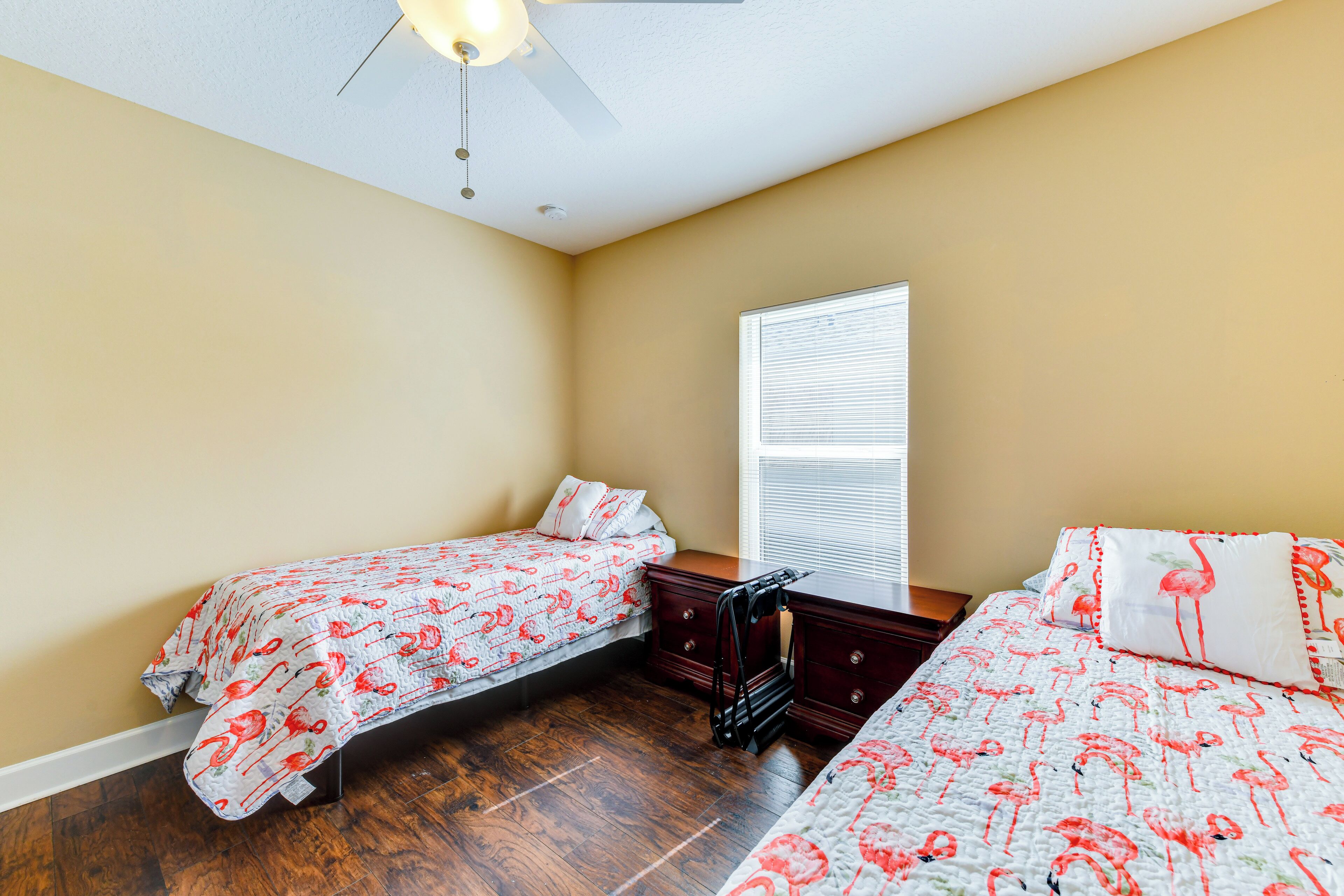 A bedroom with two beds, a ceiling fan, a window with blinds, and a wooden dresser.