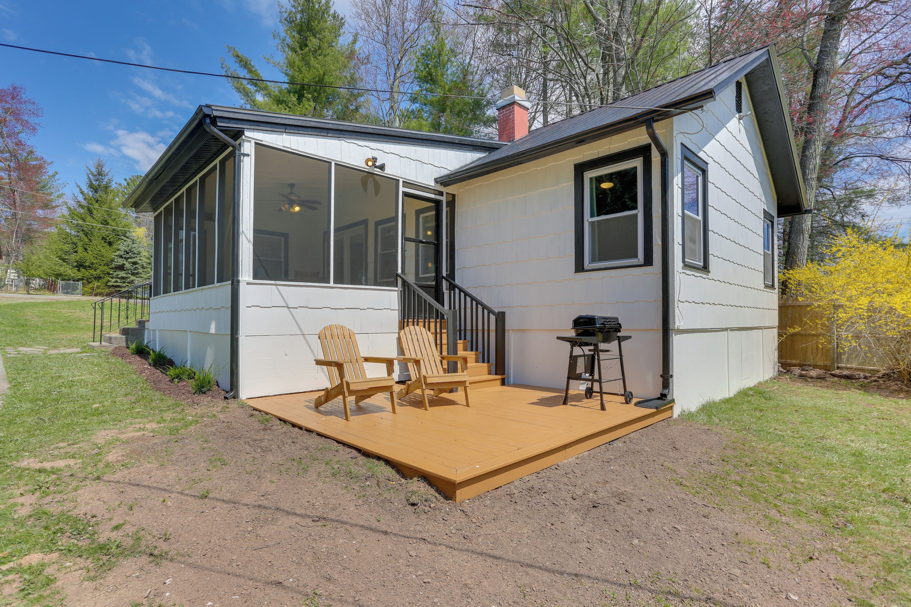 A small house with a covered patio, two Adirondack chairs, and a grill.