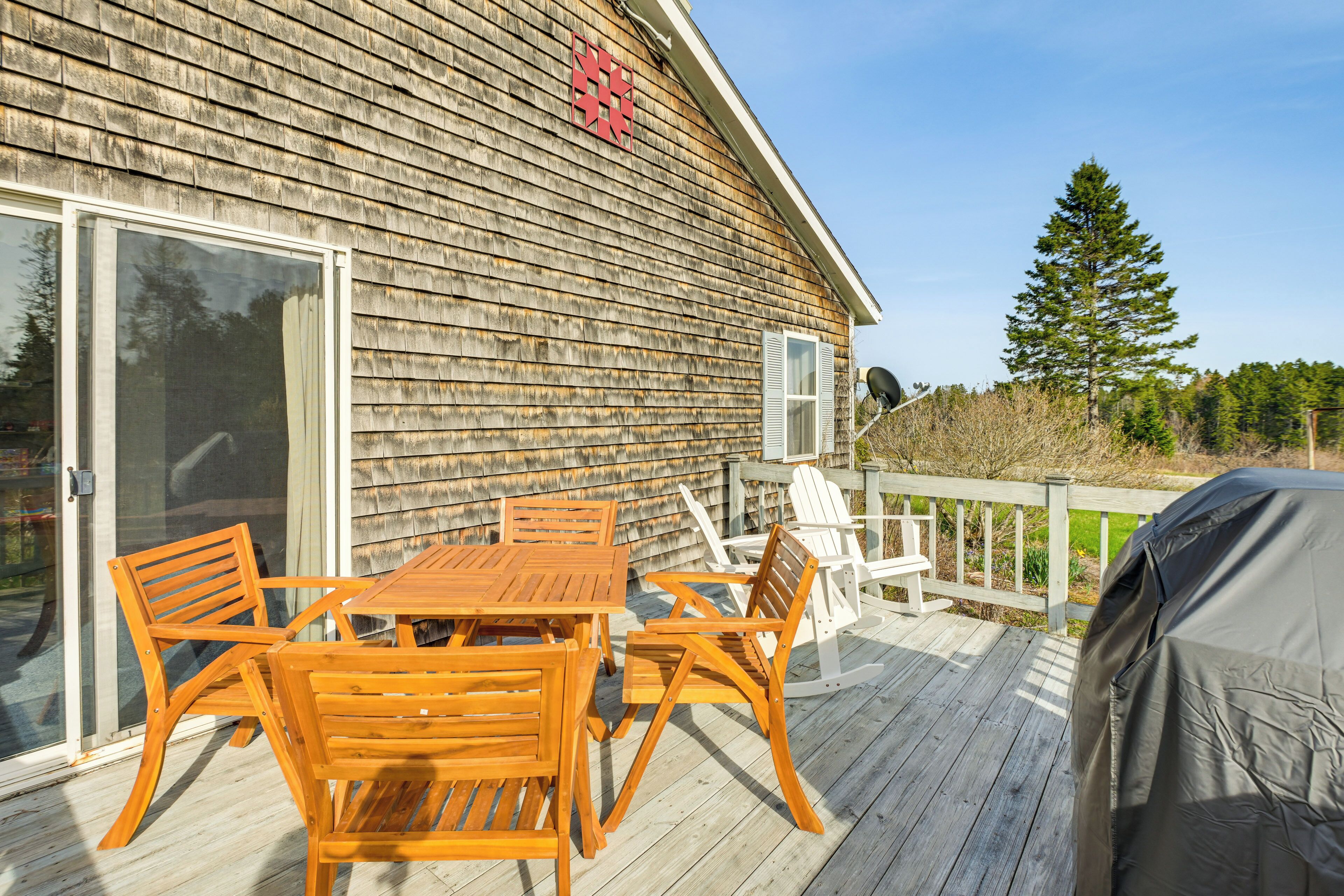 A wooden deck with a table and chairs, a covered grill, and a sliding glass door.
