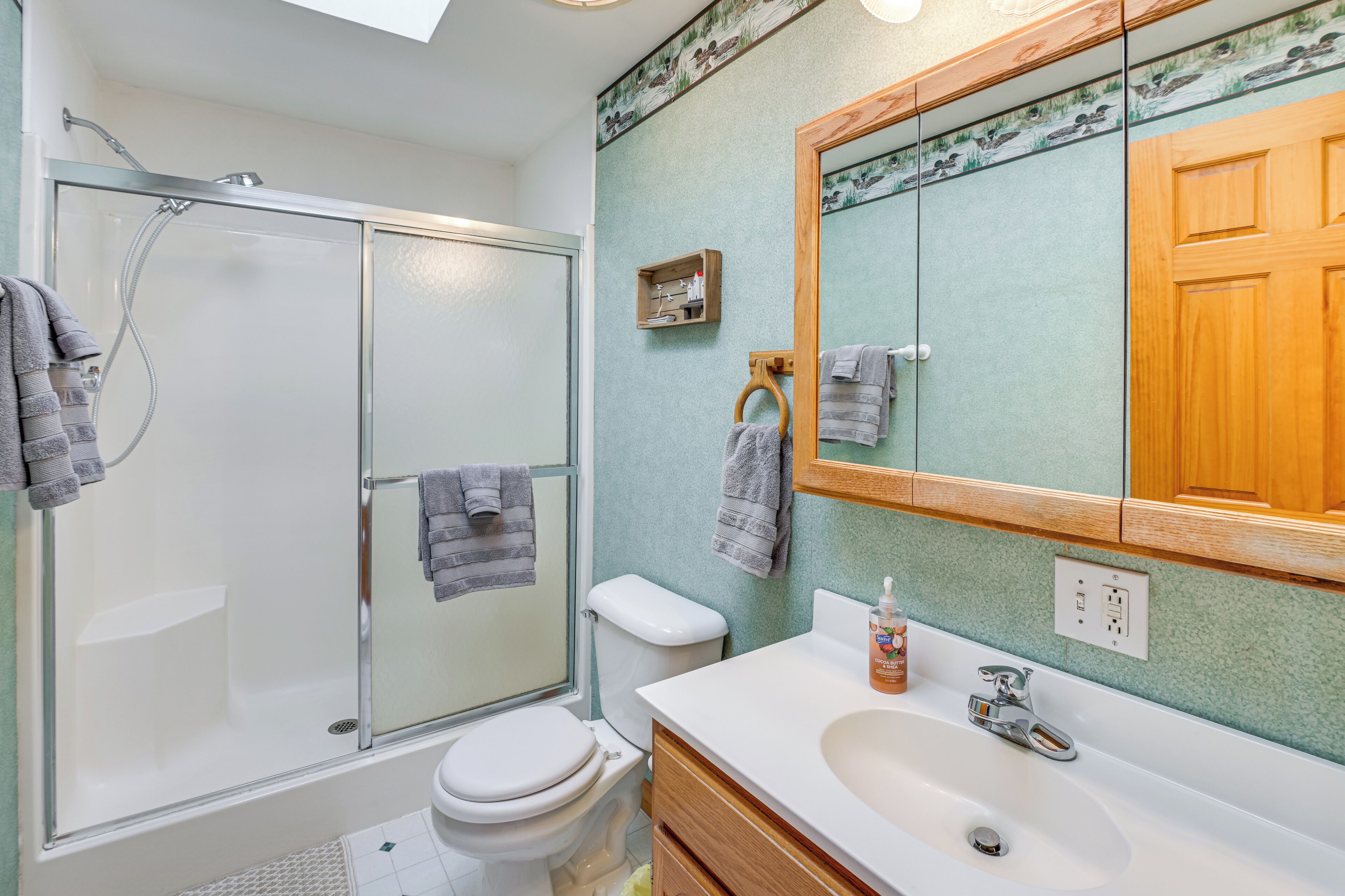 A bathroom with a glass-enclosed shower, a white toilet, a wooden vanity with a sink, and a mirror with a wooden frame.