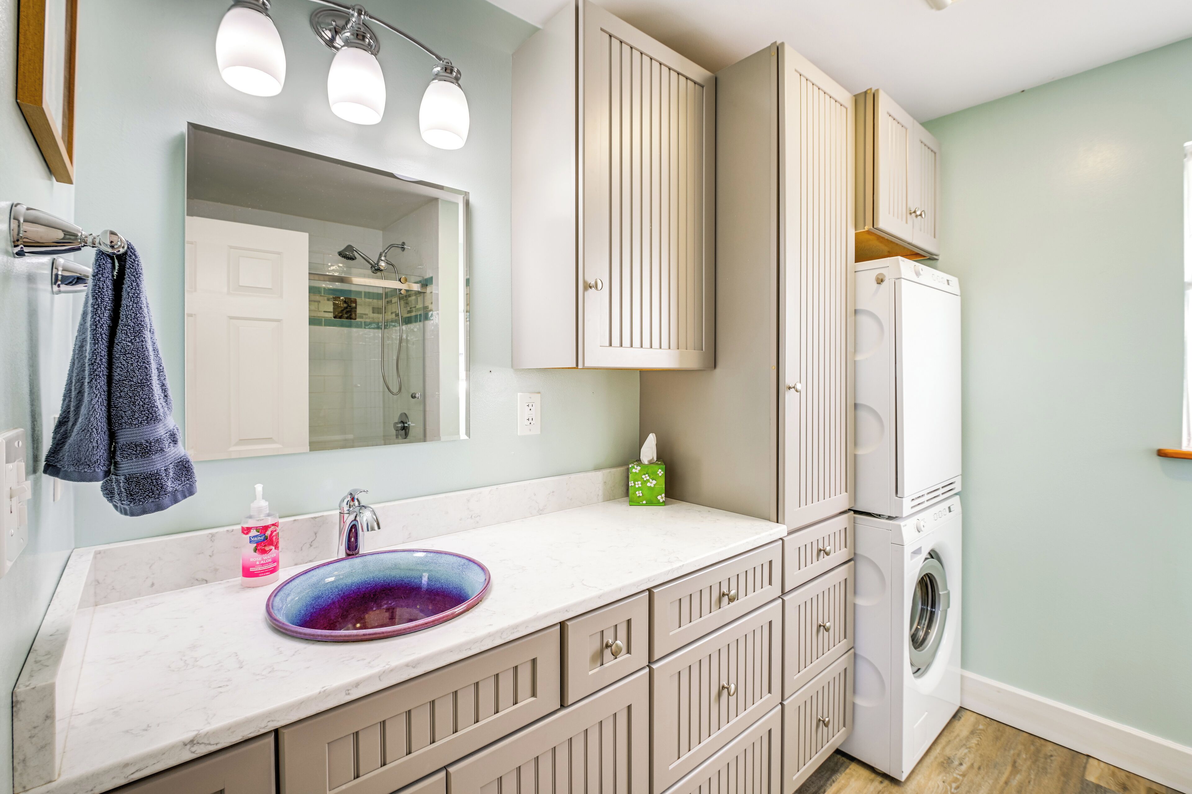 A bathroom with a sink, mirror, towel rack, cabinet, and a washing machine.