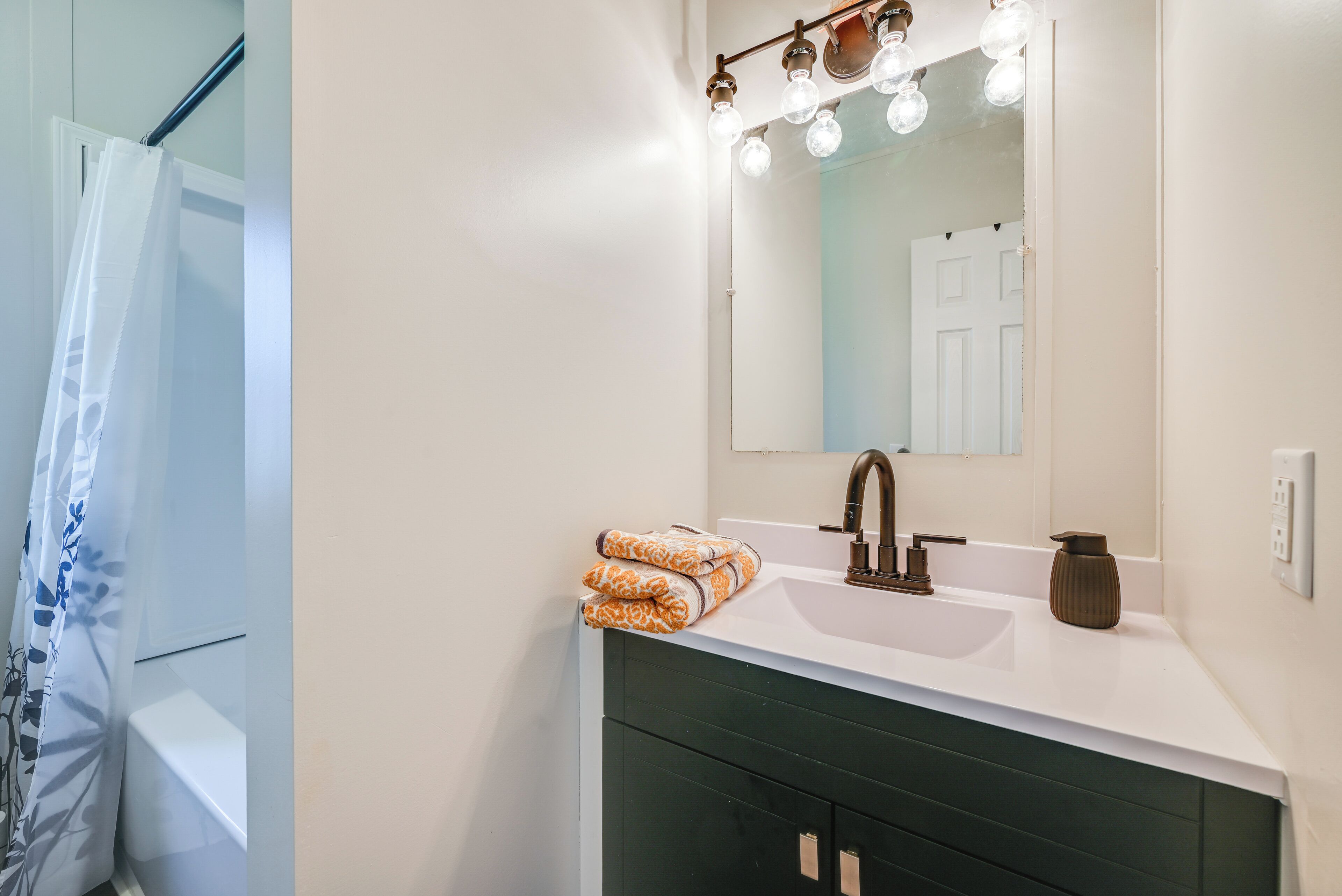A bathroom with a white sink, dark green cabinet, and a mirror with lights.