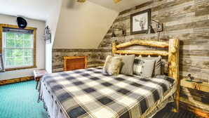 A bedroom with a wooden headboard, a checkered bedspread, a ceiling fan, a window with a view of trees, and a rustic wall design. - 'the Lodge at Crider Creek' Getaway on 140 Acres! (Bland)
