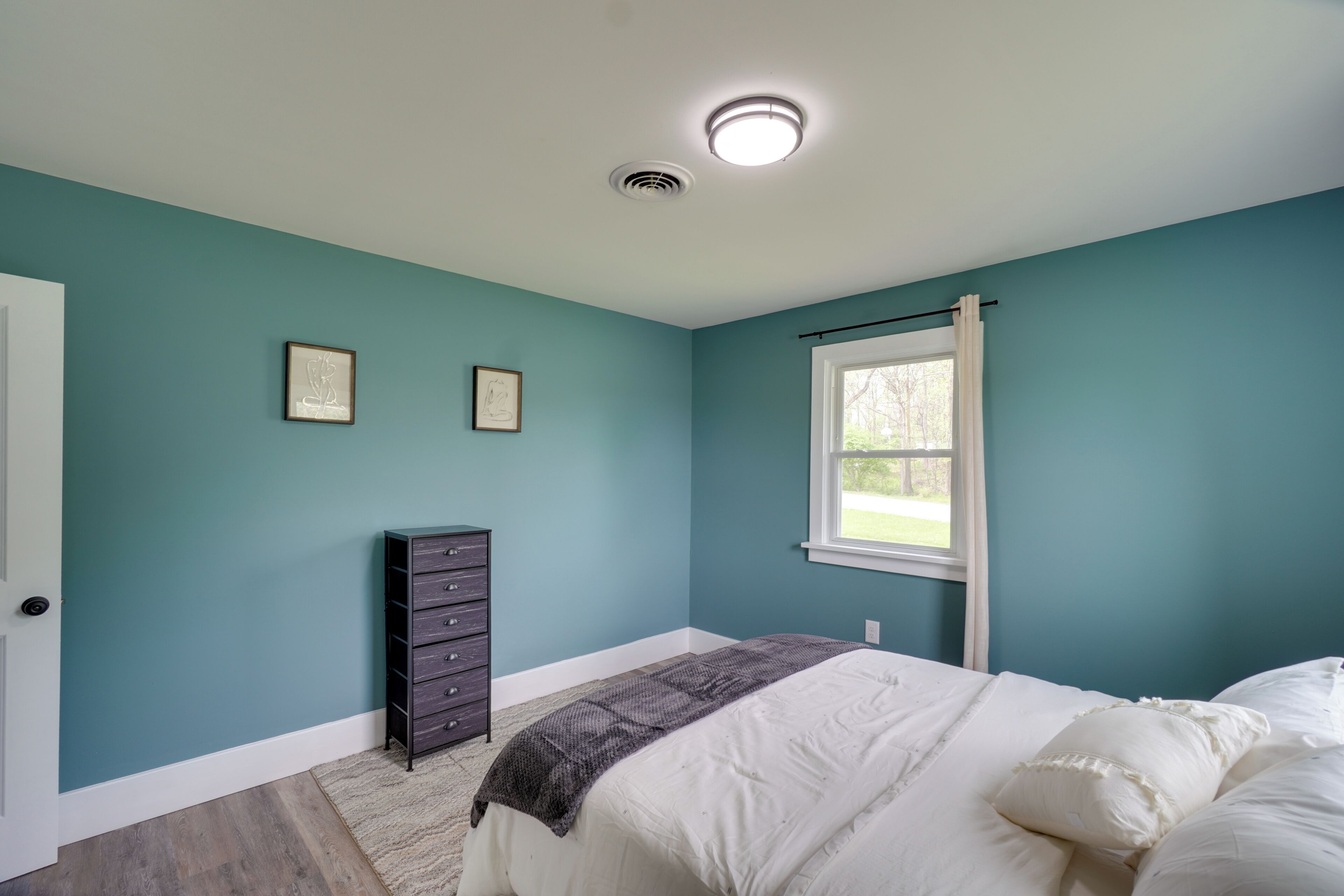 A bedroom with teal walls, a bed with white bedding, a dark dresser, and two framed pictures on the wall.