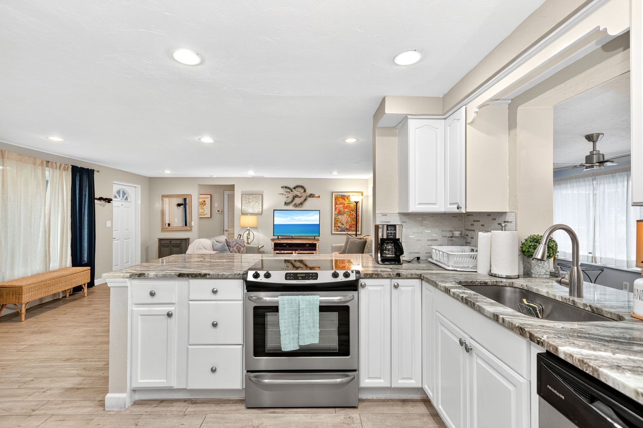 A modern kitchen with white cabinetry, a built-in oven, a stainless steel sink, and a marble countertop.